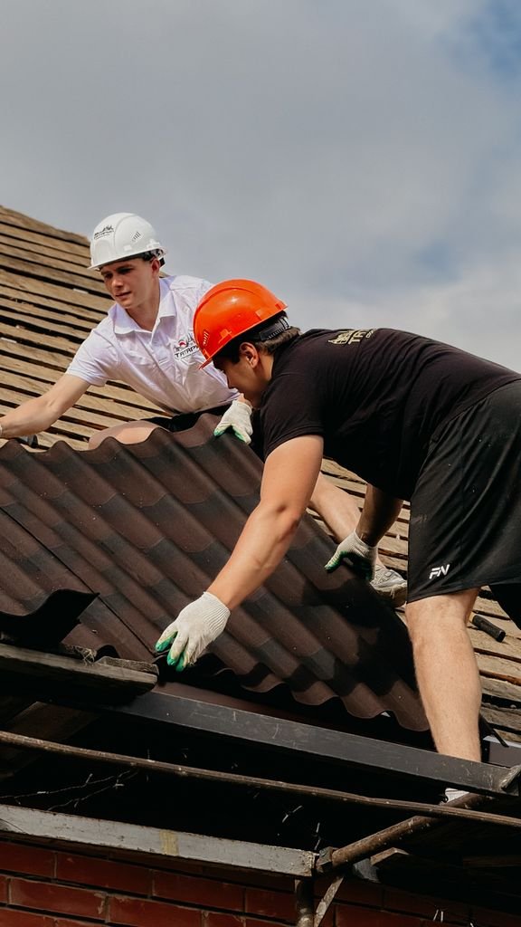 Two construction workers install roofing wearing safety helmets on a sunny day.
